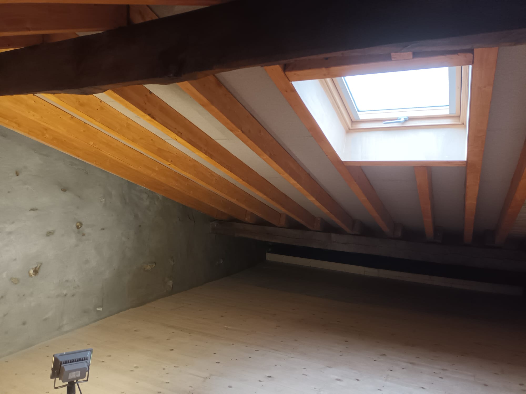 Buhardilla rehabilitada con vigas de madera vistas y ventana de tejado